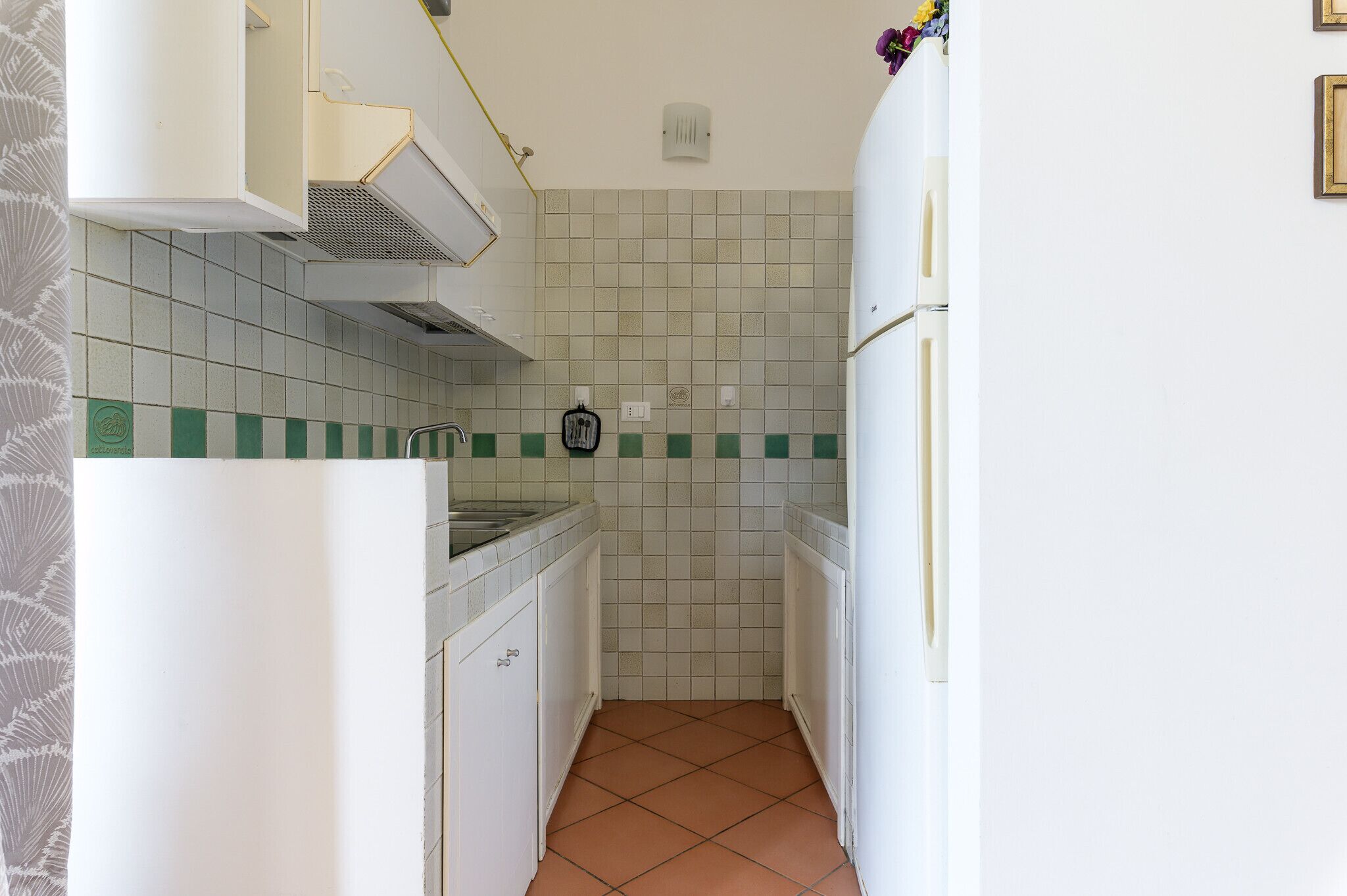 Uma cozinha compacta com armários brancos, painel de azulejos e piso revestido.