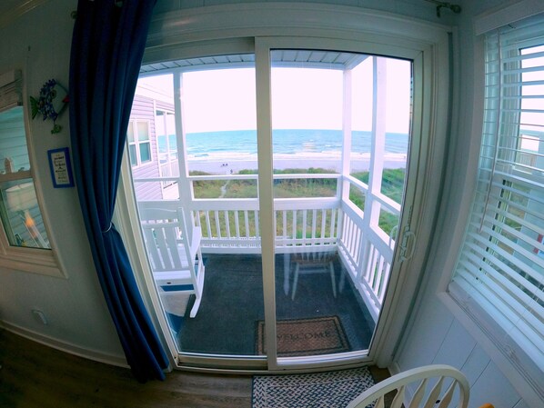 A room with a view of the beach, a door leading outside, and a small porch area.