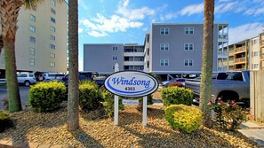 A sign for Windsong with a number 4303, surrounded by greenery and parked cars.