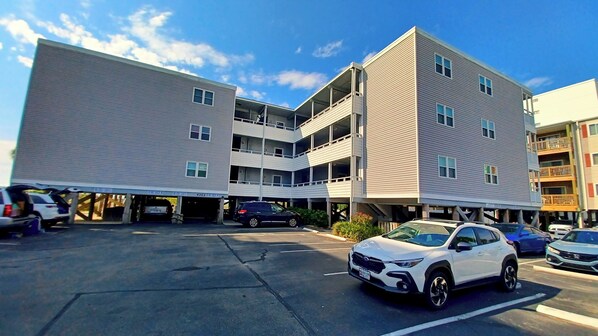 Un parking à plusieurs étages où sont garées plusieurs voitures, et un bâtiment doté d’un toit plat et de nombreuses fenêtres.