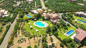 An aerial view of a resort with multiple buildings, a central swimming pool, and surrounding greenery. - Villa Dar Minzah (Aghouatim)