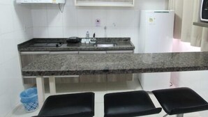 A compact kitchen with a granite countertop, a white refrigerator, and a built-in oven. There are three black stools under the counter. - LH Lacqua diRoma (Caldas Novas)