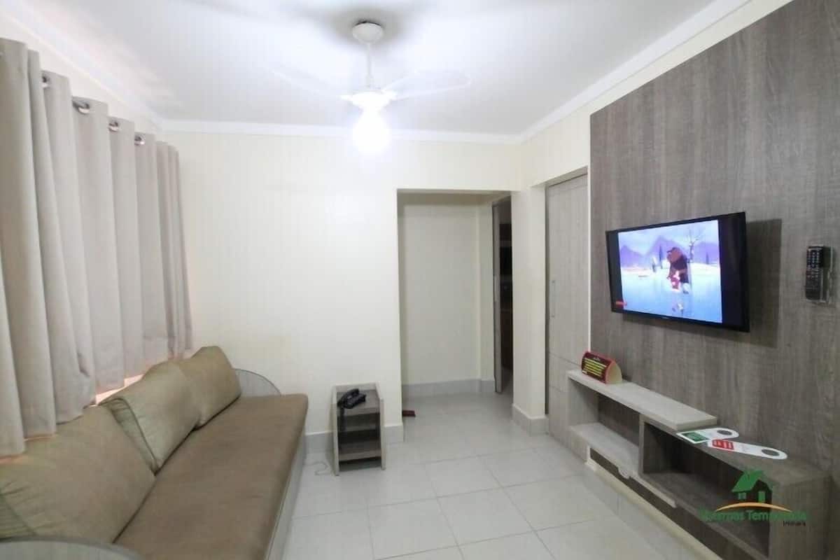 Un salon comprenant un canapé, un téléviseur fixé au mur, un ventilateur de plafond et une porte donnant sur une autre pièce.