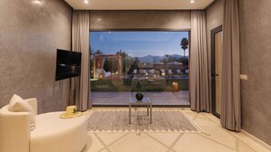 Un salon moderne doté d’un grand téléviseur, d’un canapé, d’une petite table et offrant une vue sur une piscine et des montagnes.