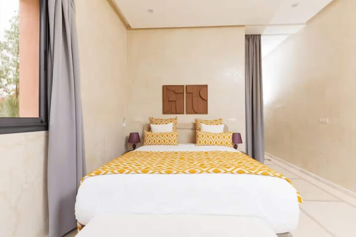 A hotel room with a bed, two nightstands, a window with curtains, and a wall-mounted artwork.