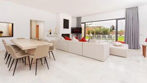 Un salon moderne comprenant un coin repas, un téléviseur à écran plat et une grande fenêtre agrémentée de rideaux.