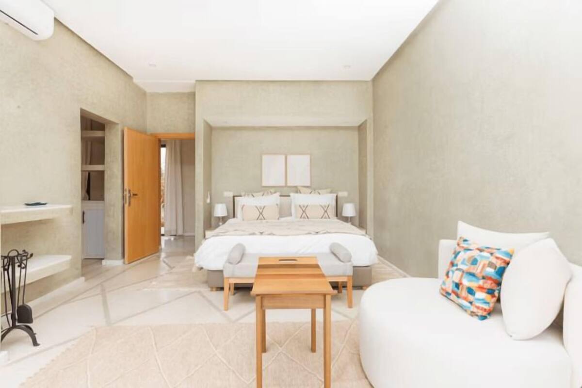 A bedroom with a bed, bedside tables, a bench, a sofa, and a small table.