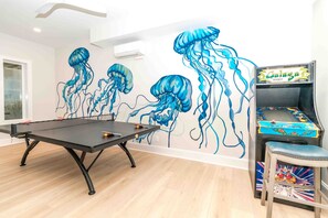 A room with a ping pong table, a wall mural of jellyfish, and a video game machine. - Ziggy's Place - New Luxury 8 BR Oceanfront Home; Pool & Elevator! (Surf City)
