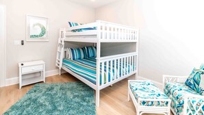 A bunk bed with a striped mattress, a small bedside table, a green rug, and a bench with a patterned cushion. - Ziggy's Place - New Luxury 8 BR Oceanfront Home; Pool & Elevator! (Surf City)