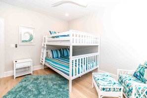 A bunk bed with a striped mattress, a small bedside table, a green rug, and a bench with a patterned cushion. - Ziggy's Place - New Luxury 8 BR Oceanfront Home; Pool & Elevator! (Surf City)