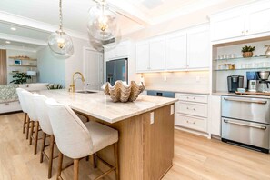 A modern kitchen with a central island, bar stools, a stainless steel oven, and a coffee maker. - Ziggy's Place - New Luxury 8 BR Oceanfront Home; Pool & Elevator! (Surf City)