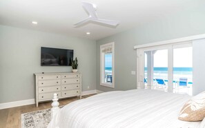 A bedroom with a bed, a dresser, a television, a plant, and a view of the beach through a sliding door. - Ziggy's Place - New Luxury 8 BR Oceanfront Home; Pool & Elevator! (Surf City)