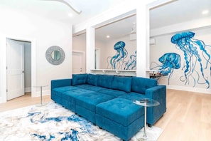 Ein modernes Wohnzimmer mit einem blauen Modulsofa, einem Glastisch und einer großen Wandmalerei von Quallen.