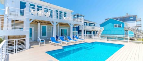 A poolside area with a swimming pool, lounge chairs, and a multi-level building with balconies.