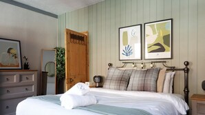 A neatly made bed with a rolled towel, a bedside table with a lamp, and two framed artworks on the wall. - Ashley Suite by Koya Homes (Vale of Glamorgan)
