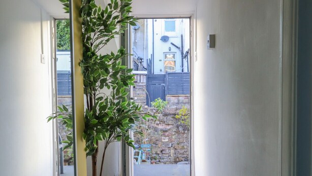 A hallway with a plant, a welcome mat, and a view of a courtyard with a stone wall and a blue door. - Ashley Suite by Koya Homes (Vale of Glamorgan)