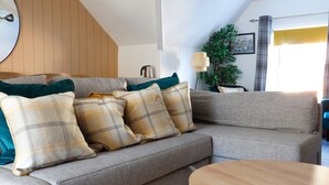 A cozy living room with a grey sofa, plaid cushions, a round wooden coffee table, a floor lamp, and a potted plant. - Ashley Suite by Koya Homes (Vale of Glamorgan)