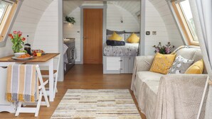 A cozy, well-lit attic bedroom with a bed, a sofa, and a dining area. - Under Oak Pod (Totnes)