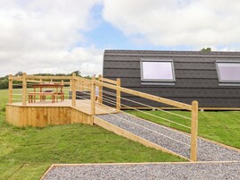 Una terraza de madera con un puente de cuerda que lleva a una plataforma elevada con una mesa y sillas.
