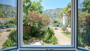 A view through a window of a garden with a mountain in the background. - Apartment Seaside (Unknown)
