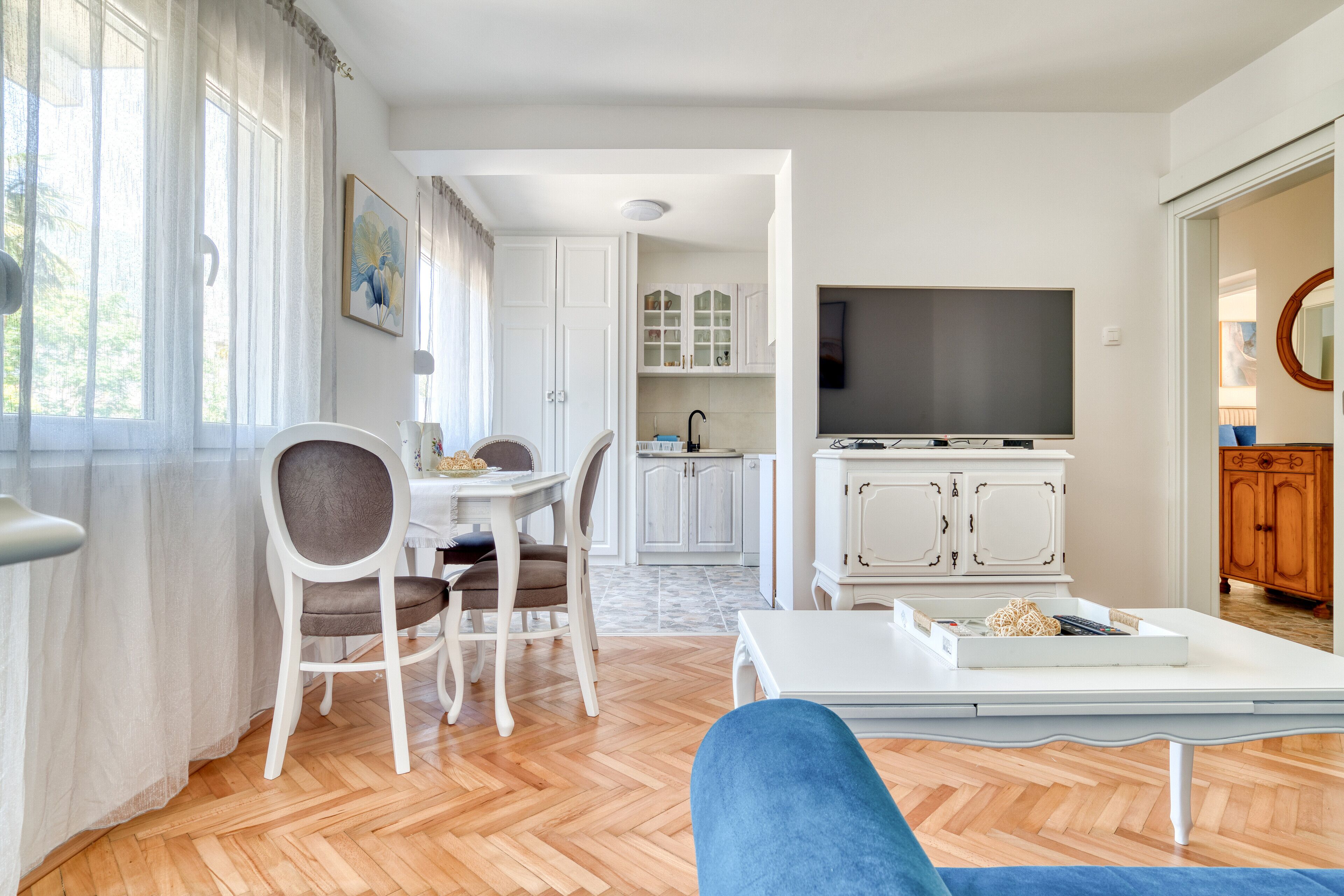 Uma sala de estar com sofá, um espaço de refeições com cadeiras, uma cozinha com armários e uma televisão.