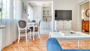 A living room with a sofa, a dining area with chairs, a kitchen with cabinets, and a TV. - Apartment Seaside (Unknown)