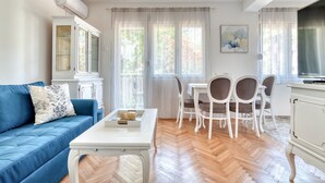 A living room with a blue sofa, white coffee table, and a dining area with white chairs and a table. - Apartment Seaside (Unknown)
