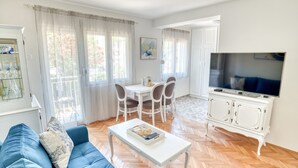 Een woonkamer met een bank, salontafel, televisie, eettafel, stoelen en een kast.