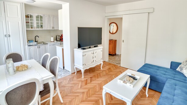 A modern living room with a blue sofa, white dining table, and a TV on a white cabinet. - Apartment Seaside (Unknown)