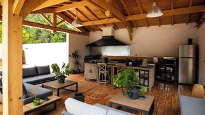 An open-plan kitchen and living area with wooden beams, a large stove, and a refrigerator. - Domaine de l'Insoupçonnée (Noves)