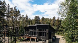 A modern two-story cabin with a deck, surrounded by dense forest. - Summer Getaway | Hot Tub, Kayaking & Mountain Biking (Saint-Côme)