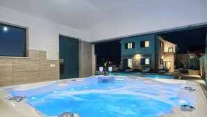 A hot tub with a stone surround, a pool, and a two-story house in the background.