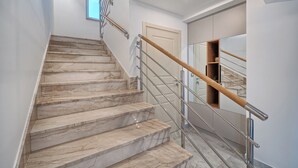 A marble staircase with metal railings and wooden handrails, leading to a room with a door and a built-in shelf.
