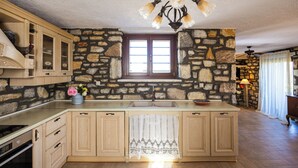 Une cuisine avec des murs en pierre, des meubles en bois, un grand îlot central et un luminaire suspendu.