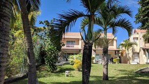 A courtyard with palm trees, a small fountain, and a building with a tiled roof. - Résidence les Banians (Grand Gaube)
