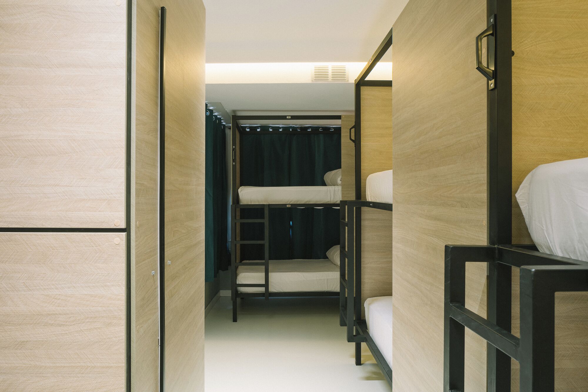 A narrow corridor with bunk beds, wooden walls, and a ceiling vent.