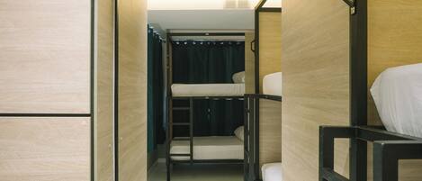 A narrow corridor with bunk beds, wooden walls, and a ceiling vent.