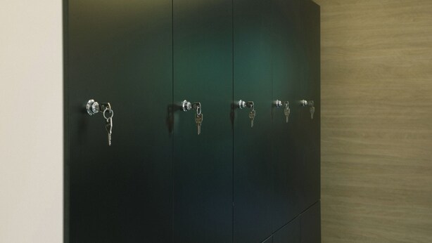 A set of dark green lockers with keys hanging on the handles. - U-nit Central Park (València)