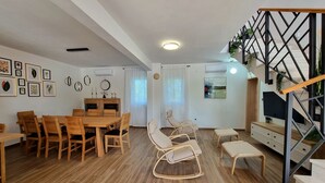 A spacious living area with a wooden dining table and chairs, a sofa, a TV, and a staircase with a geometric railing. - Villa Rosea Domus Zadarvillas (Benkovac)