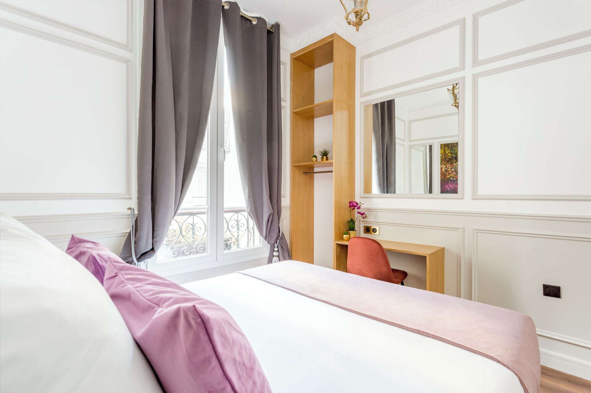 Une chambre à coucher avec un lit, un bureau, une chaise, un miroir et une fenêtre avec des rideaux.