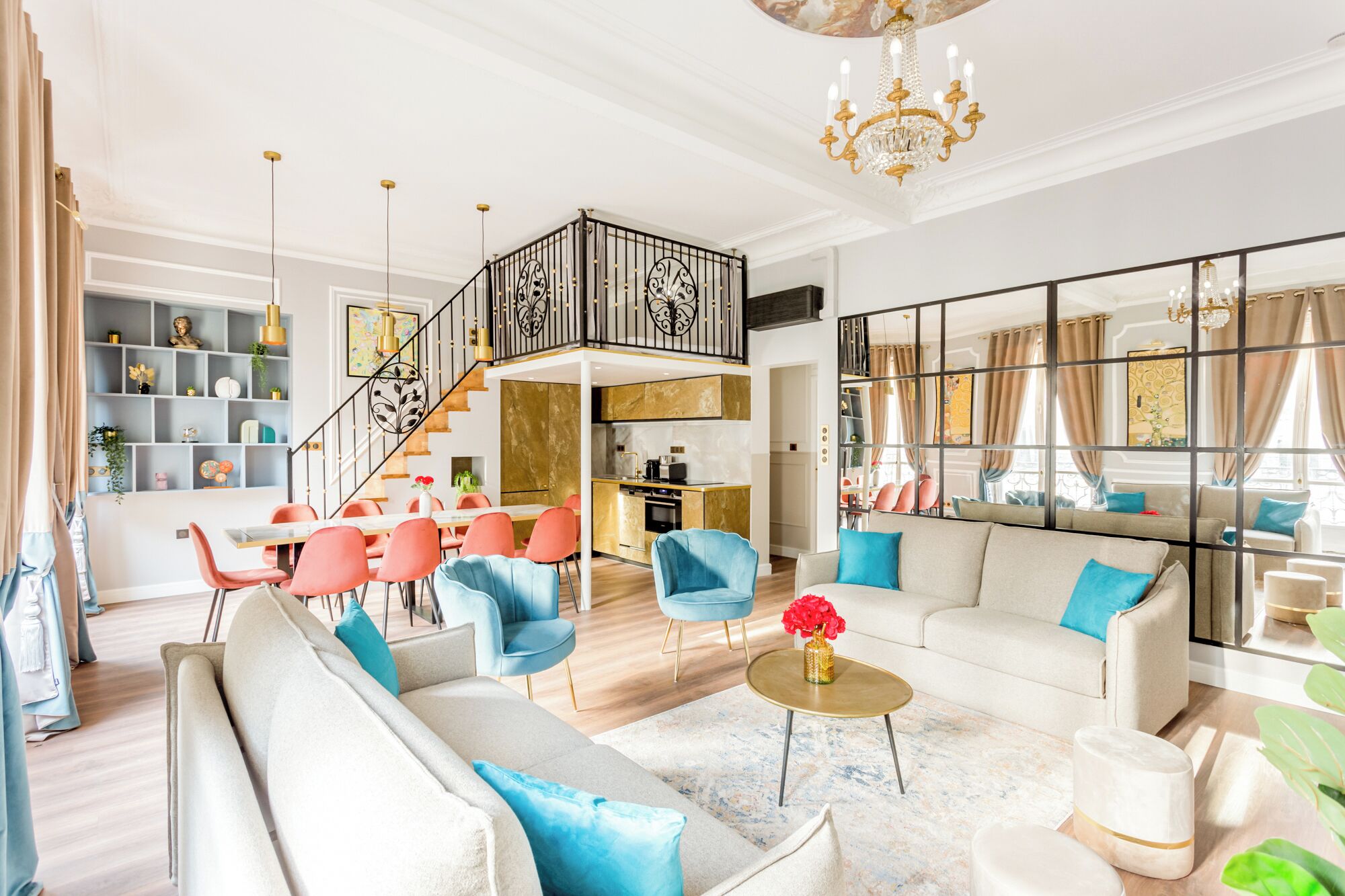 A spacious living area with a high ceiling, a staircase, and a kitchen in the background.