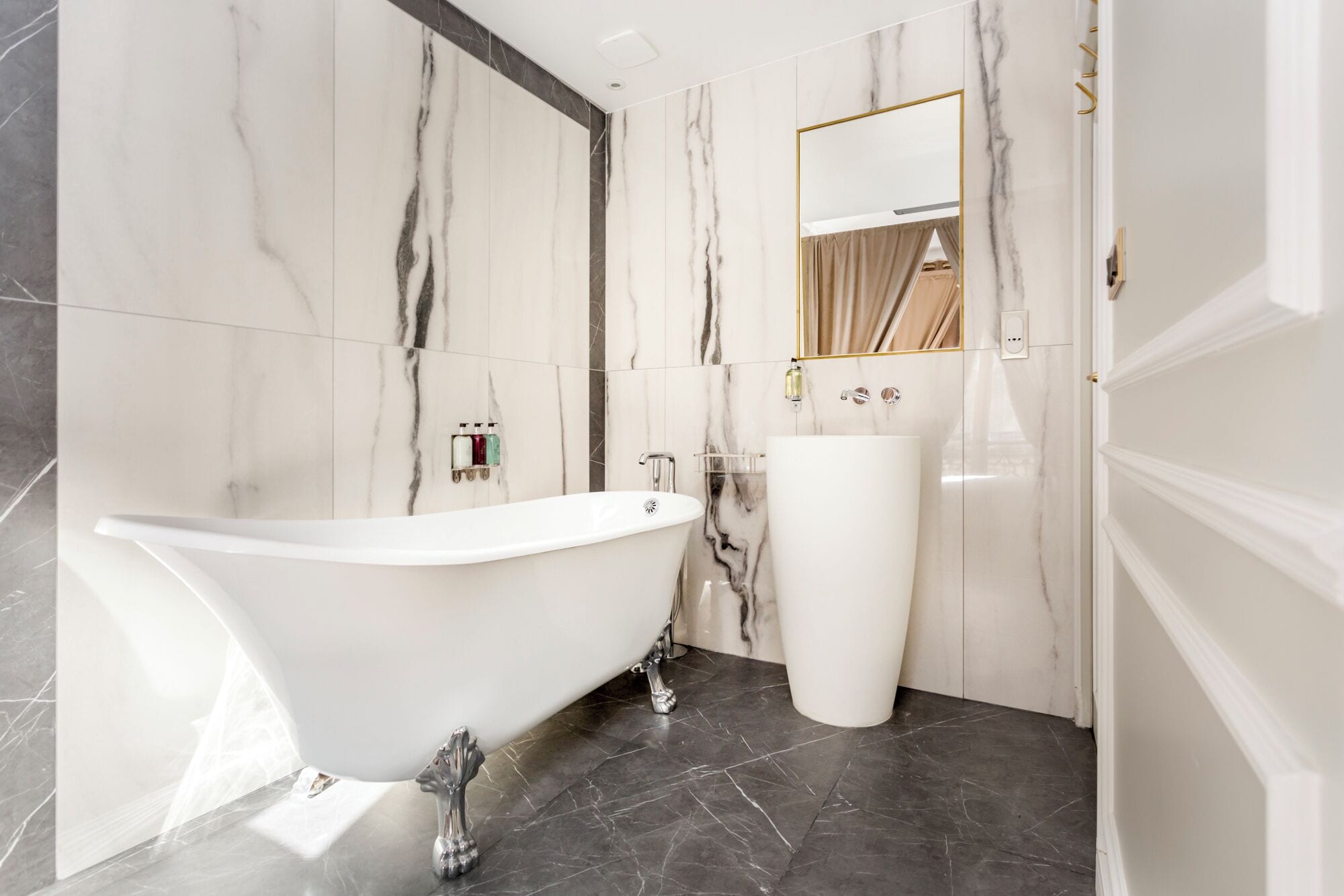 A bathroom with a freestanding bathtub, a pedestal sink, and marble walls.