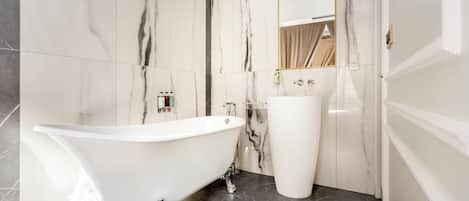 A bathroom with a freestanding bathtub, a pedestal sink, and marble walls.