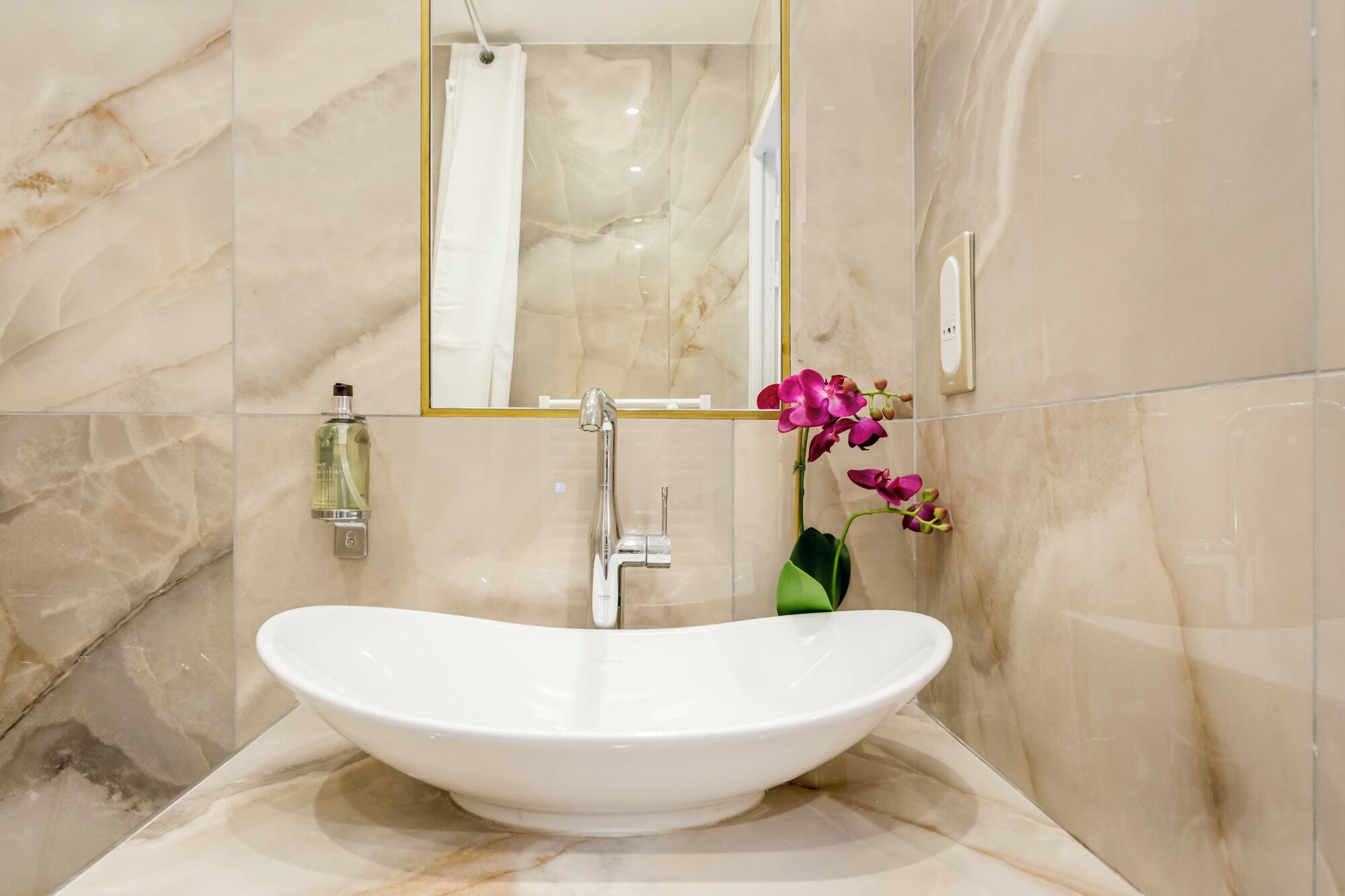 Een badkamer met een witte, ovale wastafel, een spiegel en een douche.