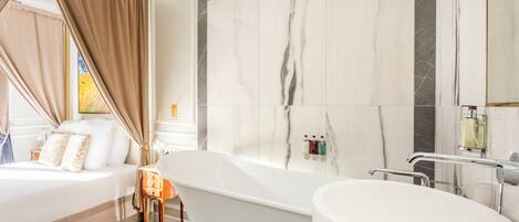 A modern bathroom with a freestanding bathtub, a large mirror, and marble walls.