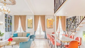A spacious living room with a sofa, chairs, a dining table, and a staircase. - Merveil Luxury Suites - Septembre I-II (Paris)