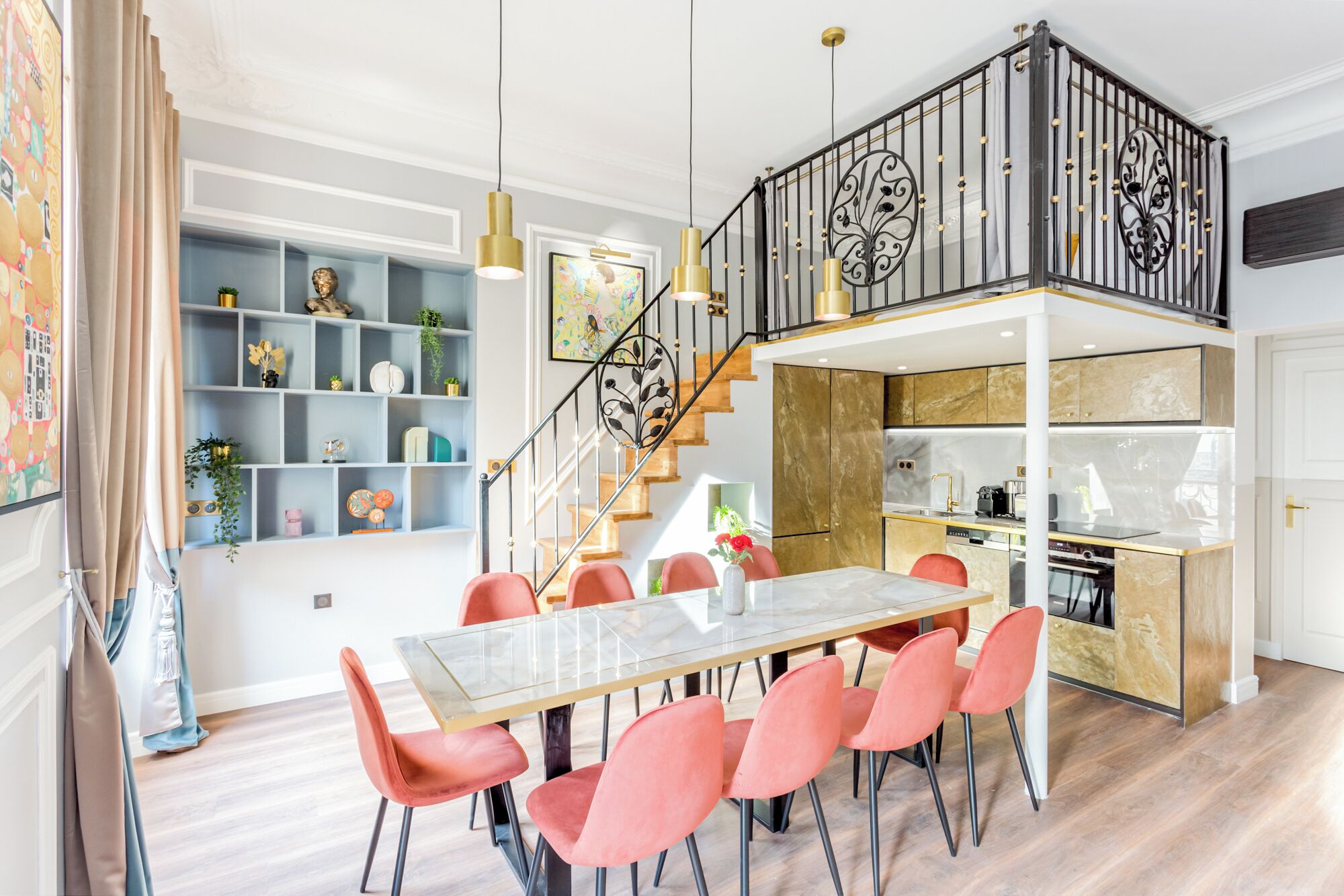 A modern kitchen with a marble countertop, a dining area with a glass table and red chairs, and a staircase with a decorative railing.