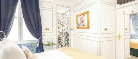 A bedroom with a bed, a chandelier, a mirror, and a bathroom with a sink and shower.