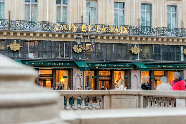 Un bâtiment sur lequel on peut lire, au-dessus de l’entrée, les inscriptions « CAFÉ de la PAIX » et « RESTAURANT CAFÉ de la PAIX ».