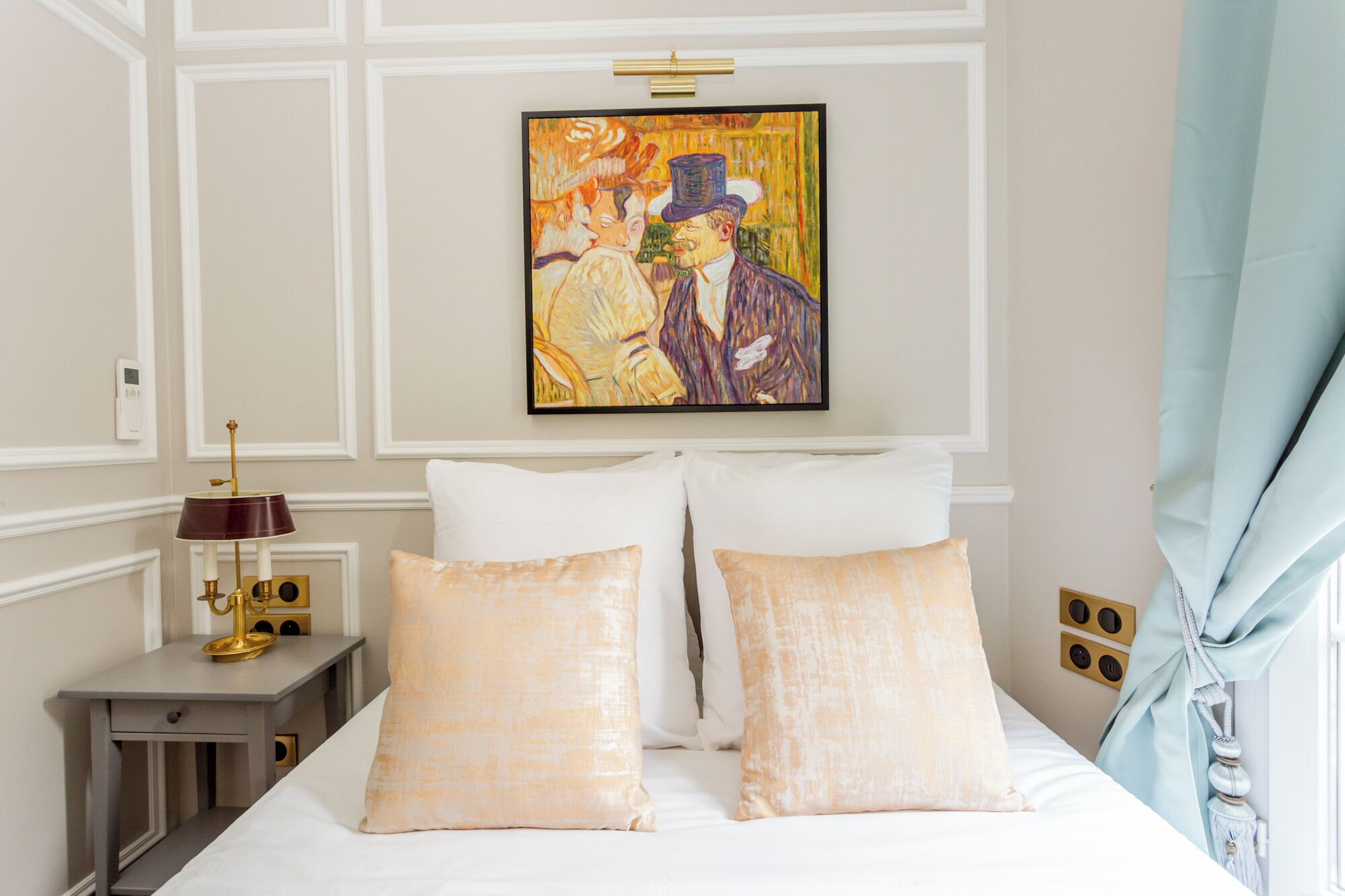 Une chambre d’hôtel avec un lit, une table de chevet avec une lampe, un tableau au mur et une fenêtre avec des rideaux.